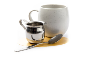 Obraz na płótnie Canvas a stainless steel creamer spoon with a coffee cup in the background isolated on white