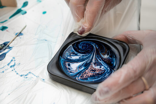 Selective focus. DIY art decoration of the cup holder with epoxy resin, colored dyes, sparkles. The master wipes the stained element with a napkin.