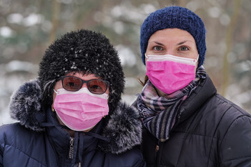 Elderly senior woman with her younger daughter in warm winter clothes, both of them wearing pink single use disposable virus face mask