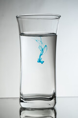 Single drop of light blue ink falling down into the glass full of water in the studio. Reflecting surface and gradient background
