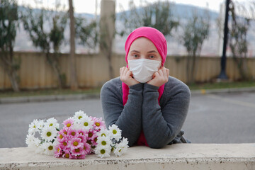 Girl in pink scarf and white mask with daisies outdoors. Cancer awareness concept. 