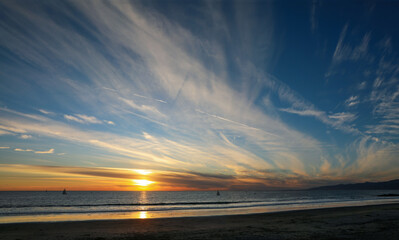 Sun setting on Venice Beach with airplane contrails and sailboats