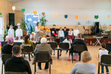Parents at the performance of children in kindergarten or school. Children on stage. Many parents are watching the kids performance in the hall during Chistmas holiday, blur. toned