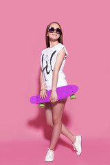 Cheerful young girl with a skateboard on the pink background.