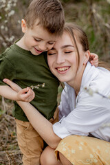 Happy mother and son having fun together. Mother gently hugs her son. In the background white flowers bloom. Mother's day