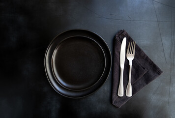 Black craft plate, cutlery and napkin on dark  table. Top view, copy space, Table setting....
