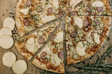 Super cheesy pizza with hunting sausages, pickles and melted cheese. sprigs of rosemary lie nearby