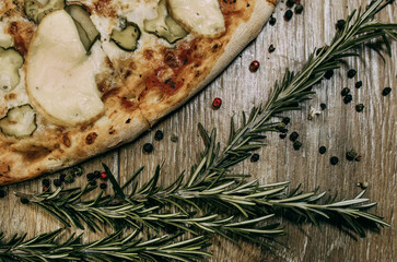 Super cheesy pizza with hunting sausages, pickles and melted cheese. sprigs of rosemary lie nearby