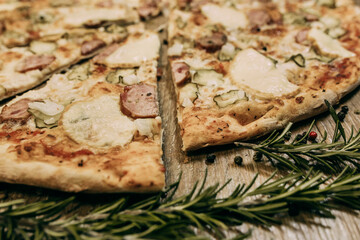 Super cheesy pizza with hunting sausages, pickles and melted cheese. sprigs of rosemary lie nearby