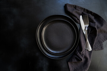 Black craft plate, cutlery and napkin on dark  table. Top view, copy space, Table setting....