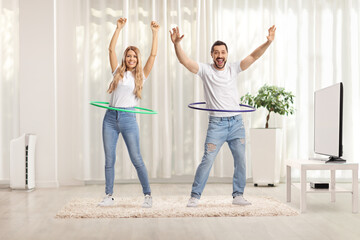 Young man and woman spinning hula hoops at home in a living room