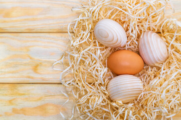 Egg and three wooden eggs in a nest with wood shavings. Idea for celebrating Easter