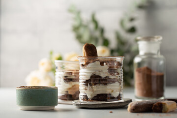 Classic italian dessert-Tiramisu in glasses with savoyardi cookies,mascarpone,cream liqueur and cocoa,with gentle flowers on background.Close-up.