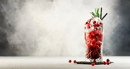Cranberry cocktail with ice, rosemary and berries in highball glass, gray background, copy space