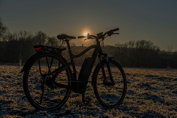 Fototapeta na wymiar Black and gray electric bicycle in sunrise morning time on frosty field