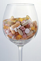 Colorful medical pills, capsules and tablets in wine glass on white background; color photo.