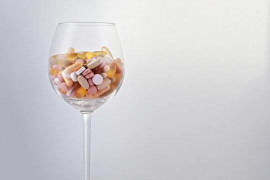 Colorful medical pills, capsules and tablets in wine glass with white background; color photo.