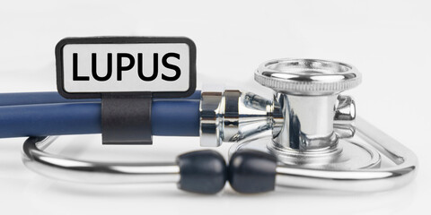 On the white surface lies a stethoscope with a plate with the inscription - LUPUS