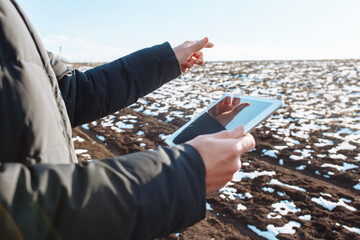 Tablet in the hands of a farmer checking the preparation process and soil readiness for seeding new crop. Farmer in the field, controlling the growth and development of wheat. Agricultural concept.