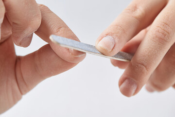 A woman does a manicure at home and uses a nail file to remove old gel polish from her nails. Close-up of a hand using a nail buffer when performing a manicure, polishing nails at home.