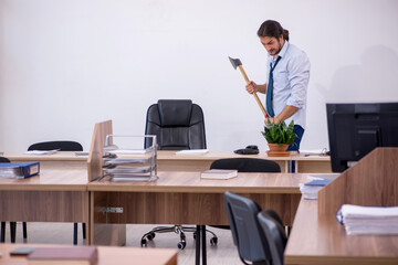 Young male furious employee holding hatchet in the office