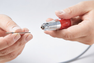 The girl changes the cutter on the machine for manicure. The girl makes a manicure at home. Cuticle treatment with a device on an isolated background. Close-up.