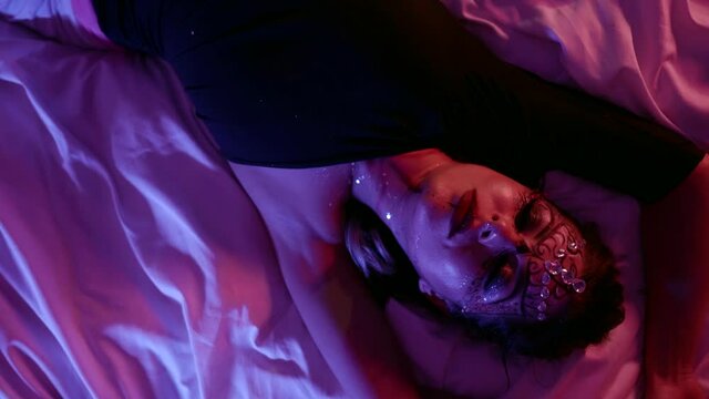 roleplay and sex entertainment, young woman with art makeup is moving seductively lying in bed in darkness