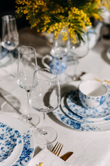 Table setting with vintage chinese porcelain tableware, mimosa flowers and wine glasses.