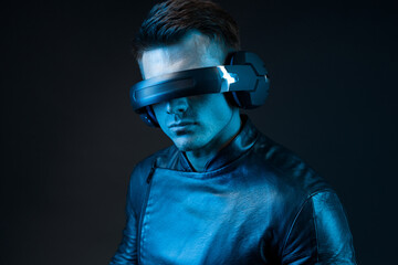 Young man in futuristic costume on dark background. Guy using VR helmet. Augmented reality, virtual...