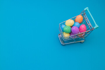 Naklejka na ściany i meble Shopping cart with easter eggs on a blue background. The concept of shopping.