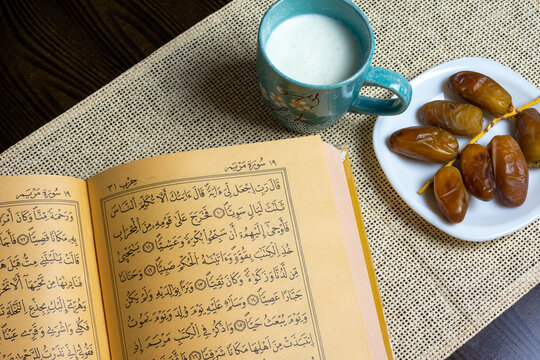 Al Quran in close up and Deglet Nour (date-palm of light) dates on a white plate with a mug of milk, Ramadan concept, space for text