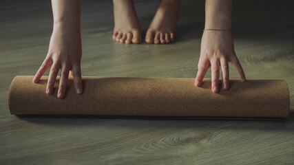 Selective light focus of woman unrolling cork yoga mat to practice yoga. Concept: self care routine practices at gome