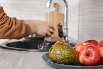 Close-up of a woman's hands washing ripe red apples and pears in the kitchen sink, placing them side by side on a plate. Selective Focus