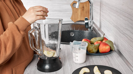 Women's hands prepare smoothies from fresh fruit using a mixer at home in their kitchen. Healthy Lifestyle Concept