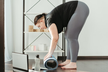 Active lifestyle, yoga trainer, flexibility, sport, fitness. Young overweight woman rolling yoga mat before workout with online trainer