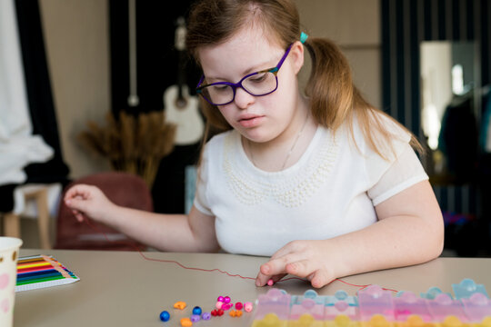 Cute Teen Girl Stringing Beads And Making Bracelet. Down Syndrome Kid Crafting Jewelry And Threading Beads. Play And Development Of Capacity  Disability Children