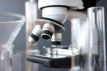 Research microscope in laboratory is next to test tubes.