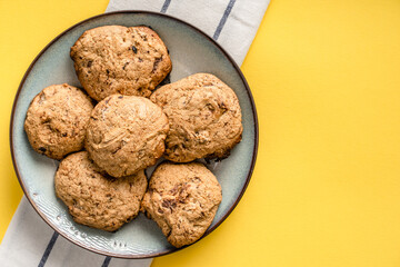 Close up top view on crunchy oatmeal chip cookies fresh baked biscuits with chocolate and cocoa in a plate on the yellow modern abstract background - homemade food concept copy space