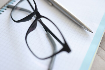 Black-framed glasses, pen, notebook lie on table