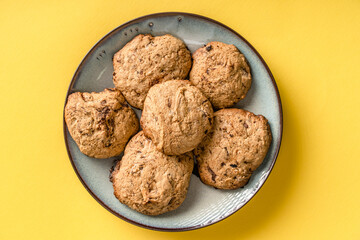 Close up top view on crunchy oatmeal chip cookies fresh baked biscuits with chocolate and cocoa in a plate on the yellow modern abstract background - homemade food concept