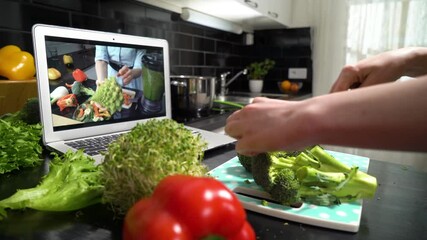 A young woman watching a online stream broadcast video blog tutorial about tasty and healthy food using laptop and cooking a meal at the home kitchen - Powered by Adobe