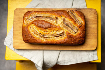 Banana bread on a wooden board, light concrete background. Linen napkin, space for text.