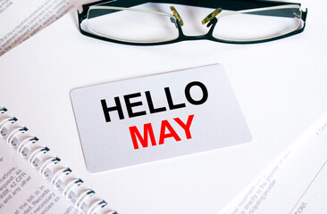 Text Hello May on a business card lying on a notepad with eyeglasses and text documents