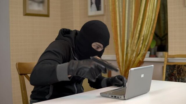 A robber is trying to hack into a laptop. A masked