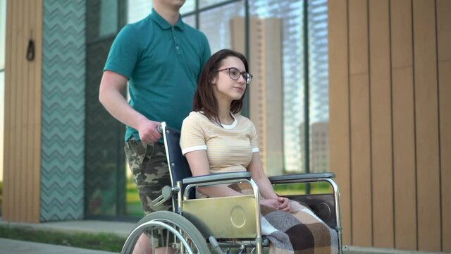 A young man carries a young woman in a wheelchair.