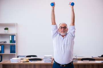 Old businessman employee doing sport exercises in the office