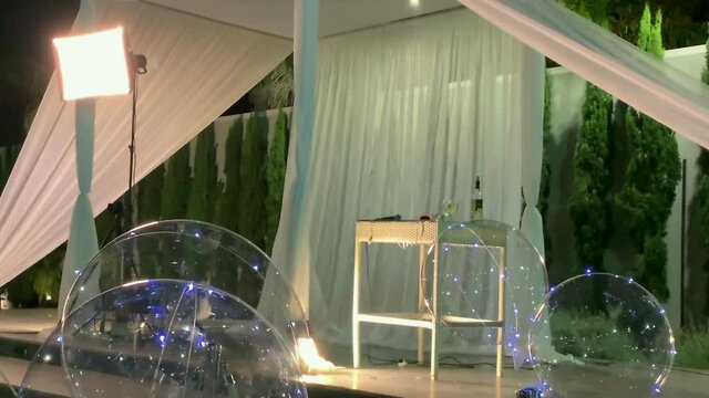 Jewish traditions wedding outdoor ceremony. Wedding canopy (chuppah, hupa) made of white fabric against the background of evening sky, palms and an artificial reservoir decorated with balloons. 4K