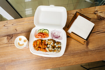Fast food made from meat, french fries and vegetables in a plastic container