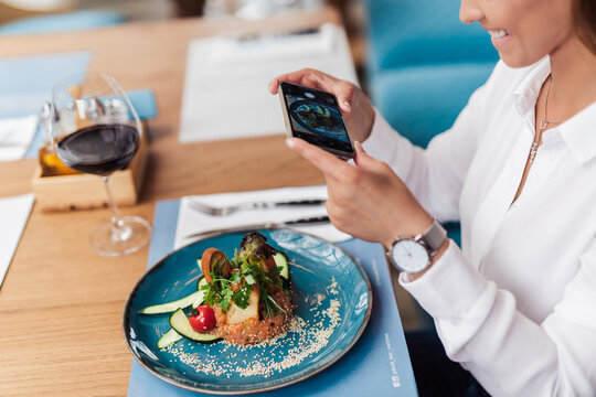 Young beautiful woman enjoying in tasty and nicely decorated meal. She sitting in expensive restaurant and using her smart phone for food photography.