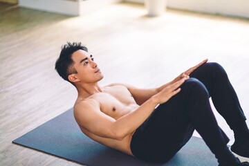 Fototapeta na wymiar Muscular Asian young man doing exercises on floor at home